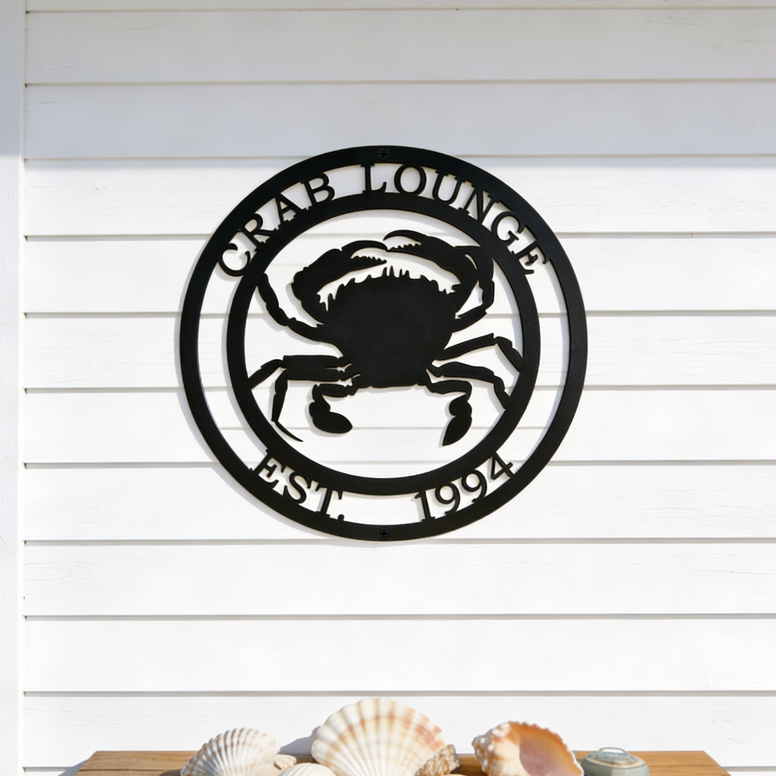 Black crab lounge metal sign with crab design displayed above seashell table decor