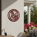Rich desert crimson finish of the personalized butterfly and rose metal art sign mounted on an outdoor white stucco column above a wooden bench with a small garden shovel and blooming hydrangeas.