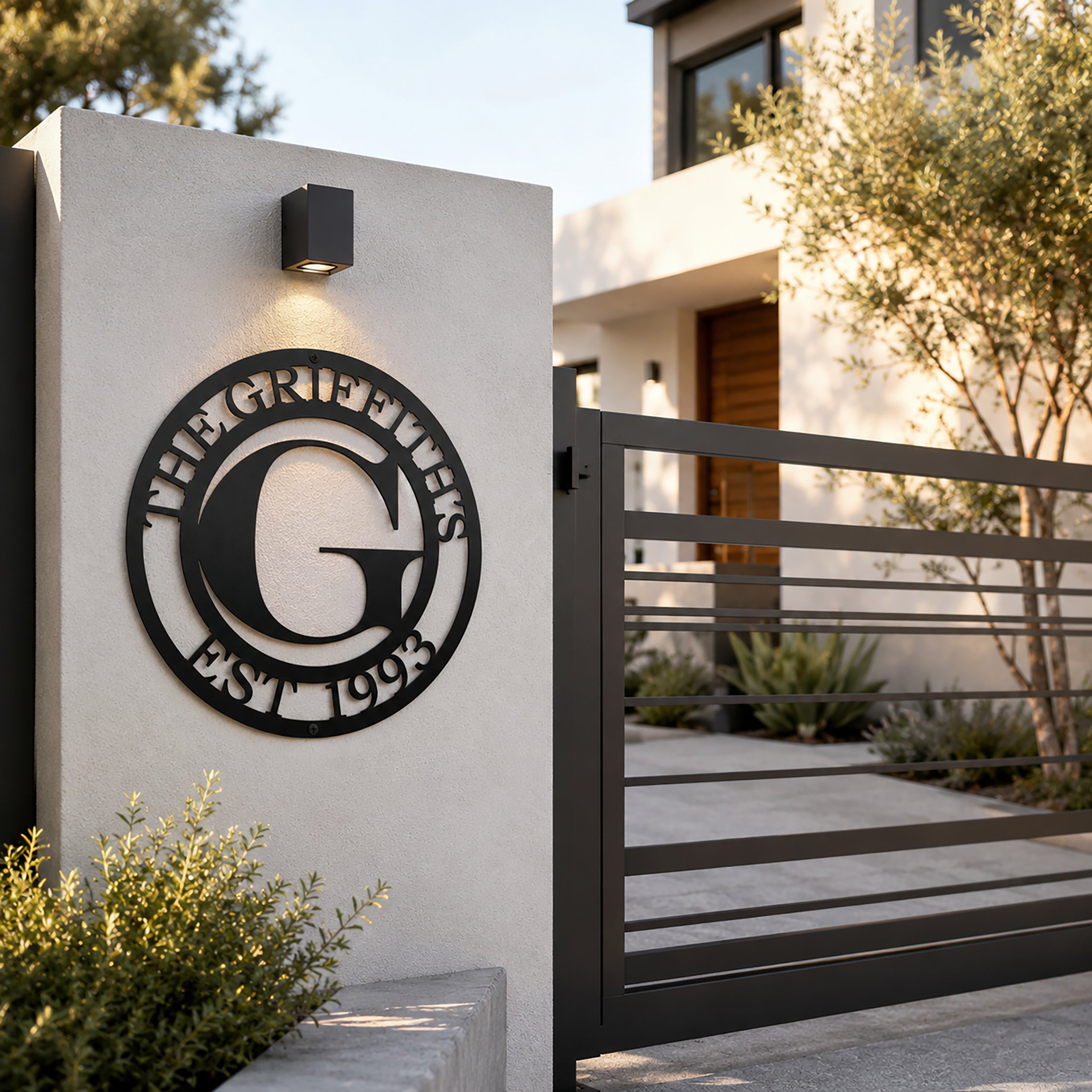 Custom family monogram metal sign — personalized satin black established sign mounted on a contemporary exterior entry wall near a modern gate.