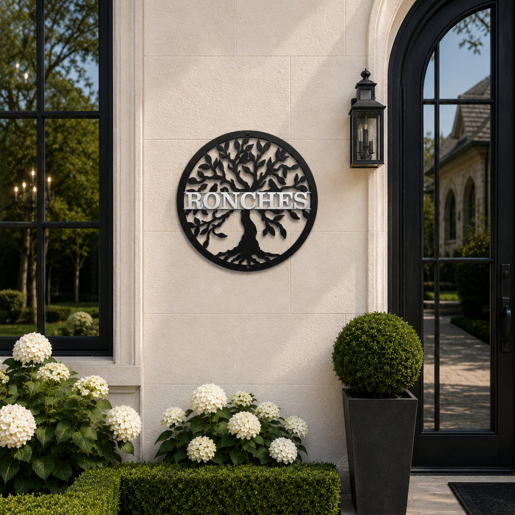 Personalized black tree monogram metal sign with custom family name displayed beside elegant outdoor entryway and garden plants