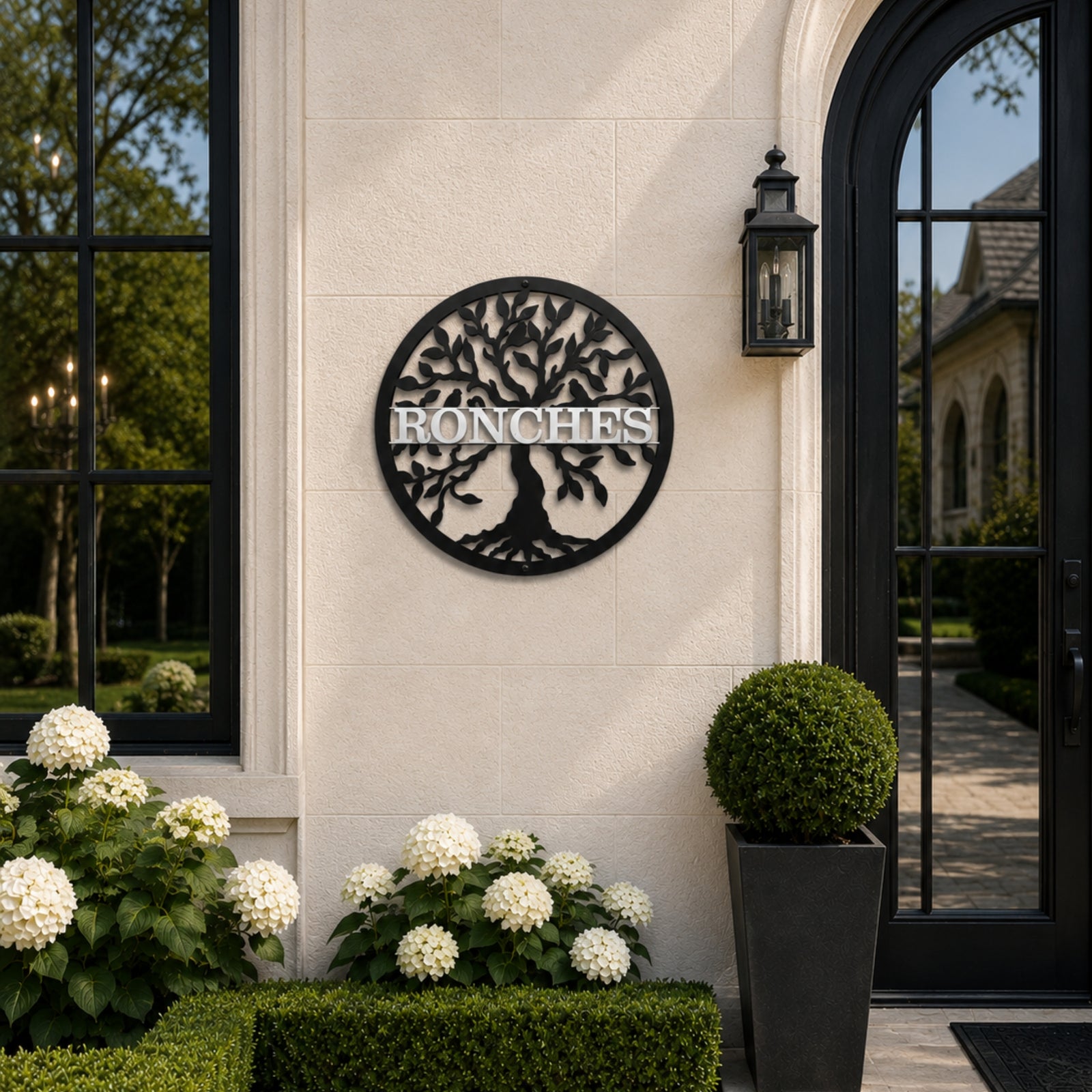 Personalized black tree monogram metal sign with custom family name displayed beside elegant outdoor entryway and garden plants