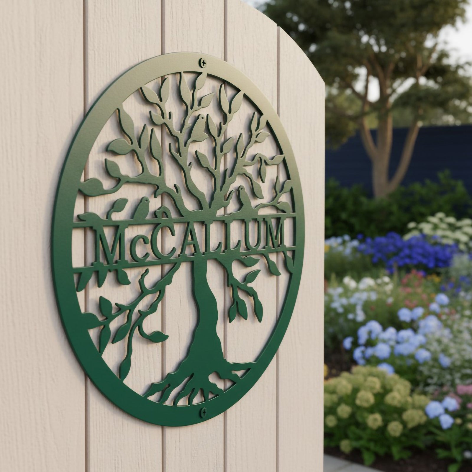 Close-up side view of a round green powder-coated steel tree of life monogram sign customized with the name McCallum on a light cream wooden fence.