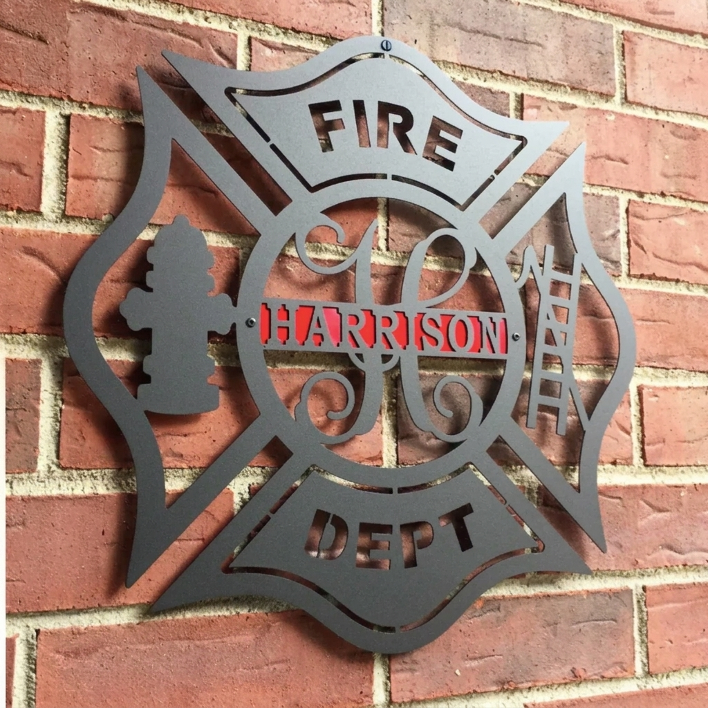 Black metal firefighter cross with a red stripe and personalized last name mounted on a red brick exterior wall.