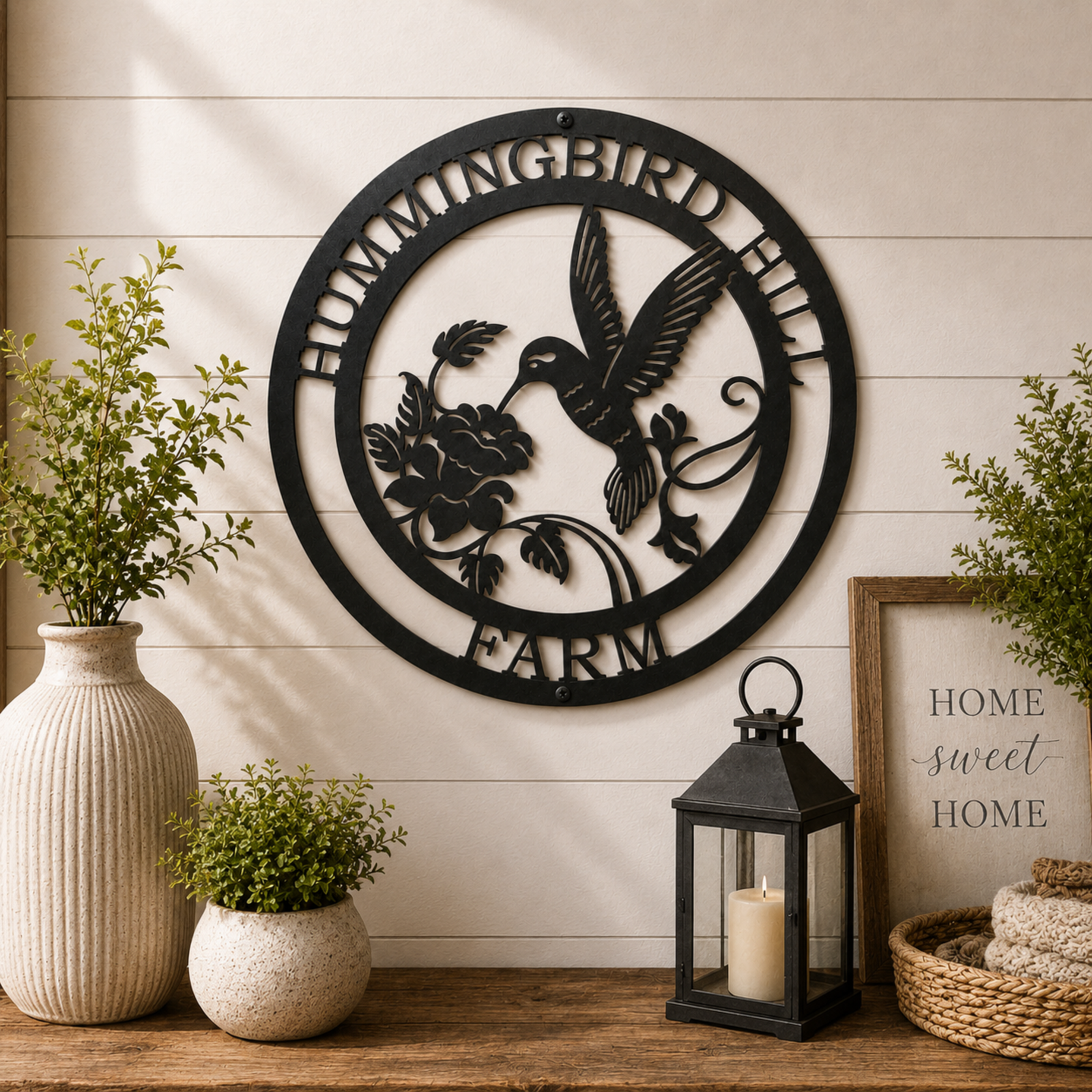 Personalized hummingbird farm metal wall décor with floral accents displayed above wooden table with lantern and plants