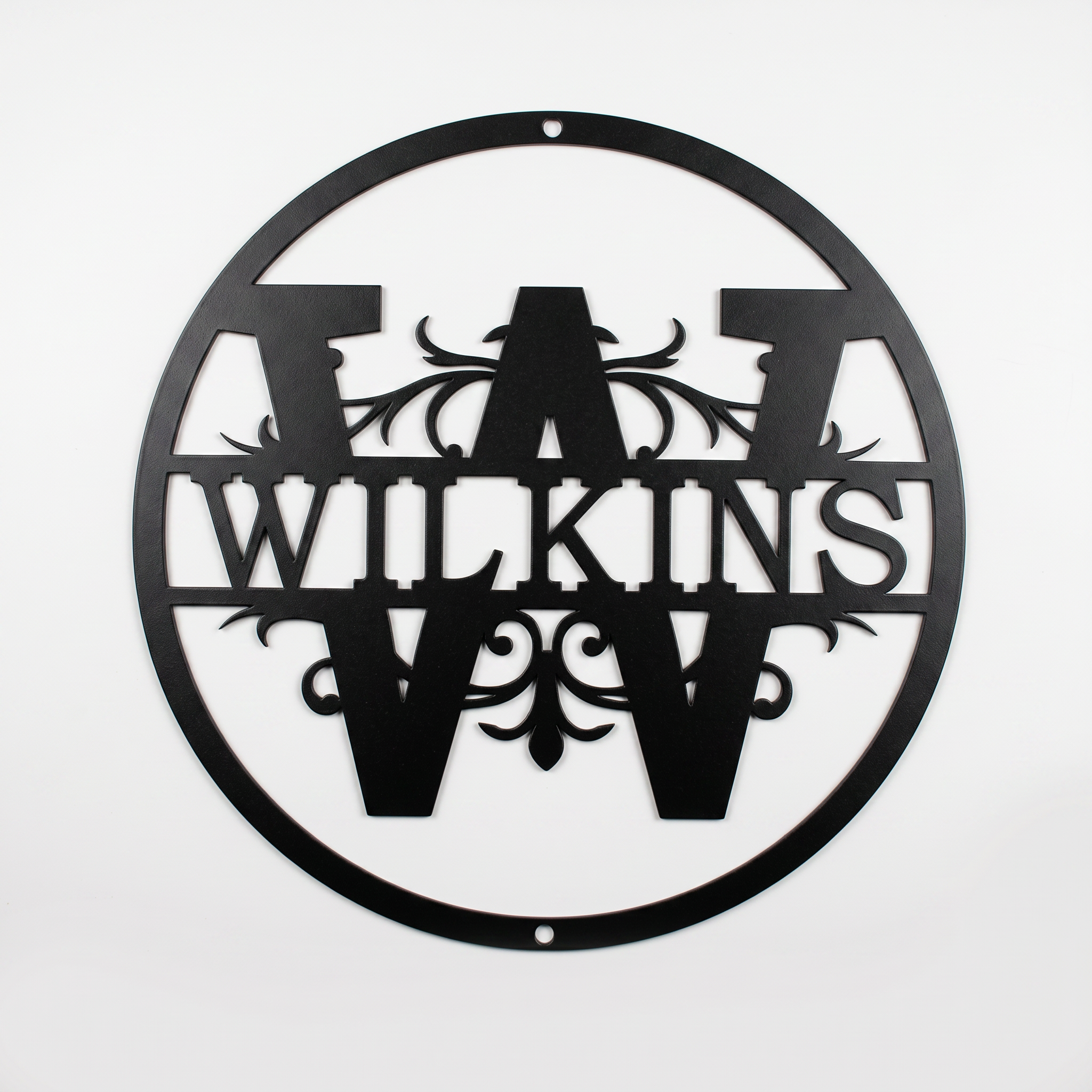 Flat view of a black circular personalized metal sign featuring a prominent letter W split monogram with elegant filigree accents and the custom surname Wilkins over a solid white background.