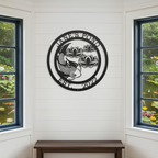 A circular black metal sign reading "Jane's Pond Est. 2022" with a detailed koi fish and lotus flowers, mounted indoors on a white shiplap wall between two large windows.