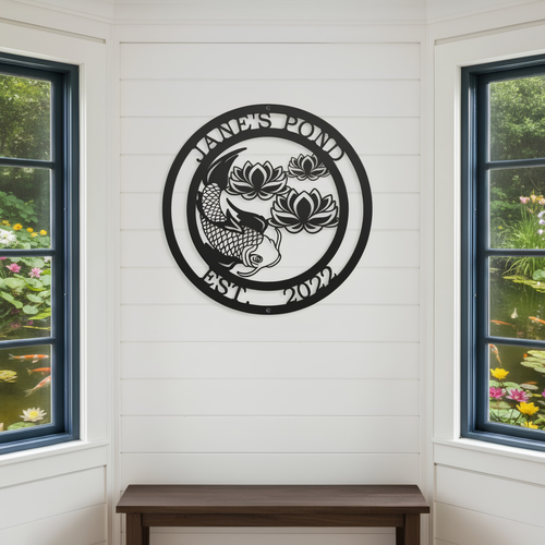 A circular black metal sign reading "Jane's Pond Est. 2022" with a detailed koi fish and lotus flowers, mounted indoors on a white shiplap wall between two large windows.