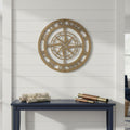 A gold circular metal compass sign customized with geographic coordinates along the outer border, mounted on a white shiplap wall above a dark blue console table decorated with rolled maps and a vintage brass telescope.
