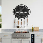Custom master griller metal BBQ wall sign with hanging grill tools displayed above outdoor cooking station and barbecue grill