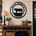 Large matte black round metal monogram sign featuring a pig and family farm text hanging on a living room wall above a wooden entryway console table.