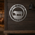 Personalized B&B Family Farms round metal sign in a brushed silver steel finish hanging on a dark rustic wooden wall inside a barn next to a vintage light fixture.