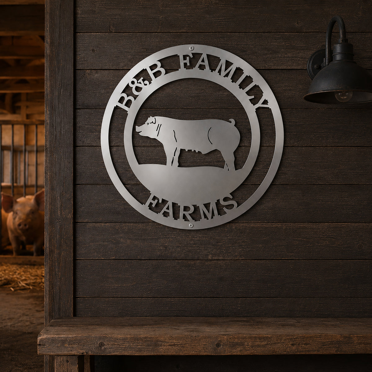 Personalized B&B Family Farms round metal sign in a brushed silver steel finish hanging on a dark rustic wooden wall inside a barn next to a vintage light fixture.