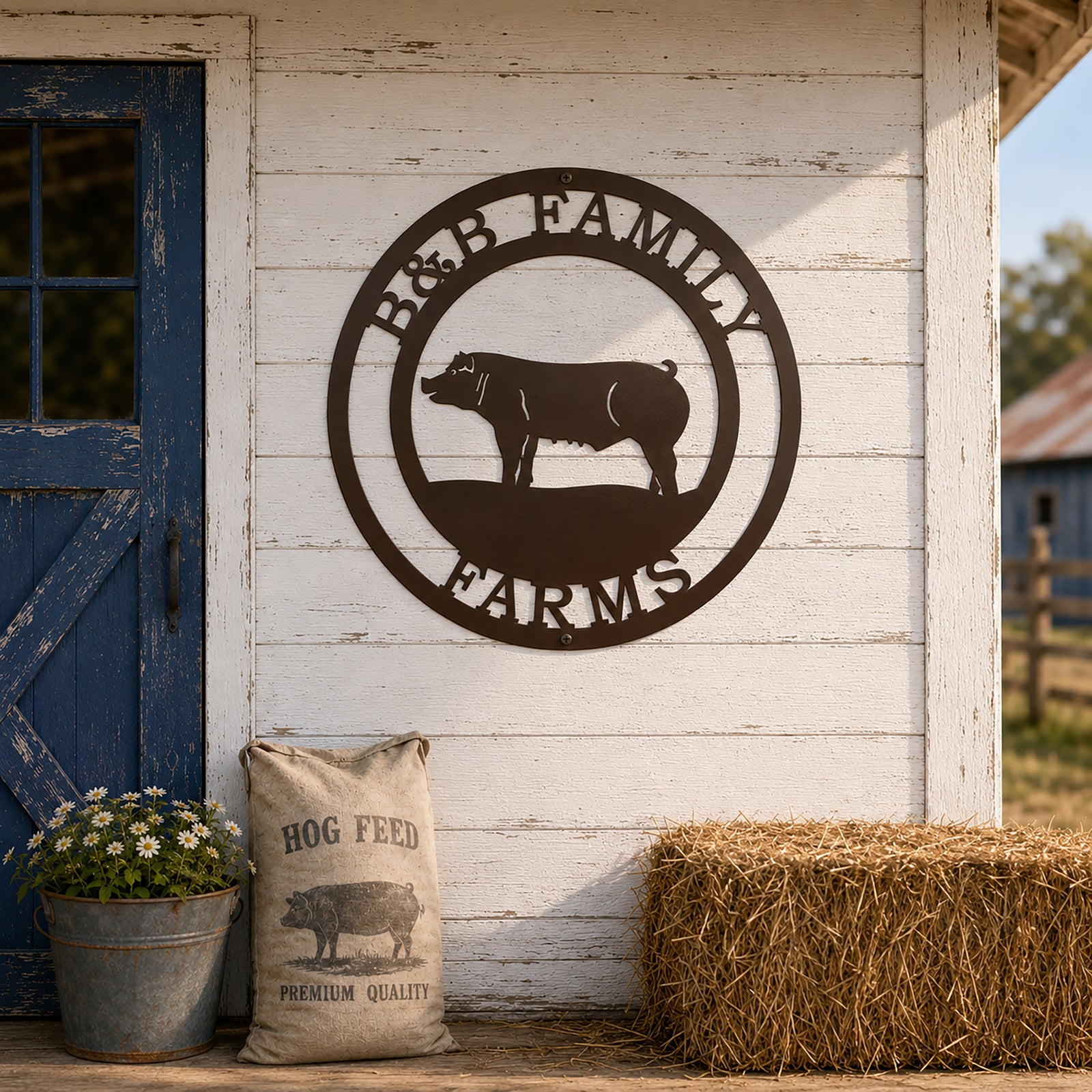 Rustic brown powder-coated metal pig farm sign reading B&B Family Farms mounted on a white wood siding wall next to a blue barn door, a bag of hog feed, and a hay bale.