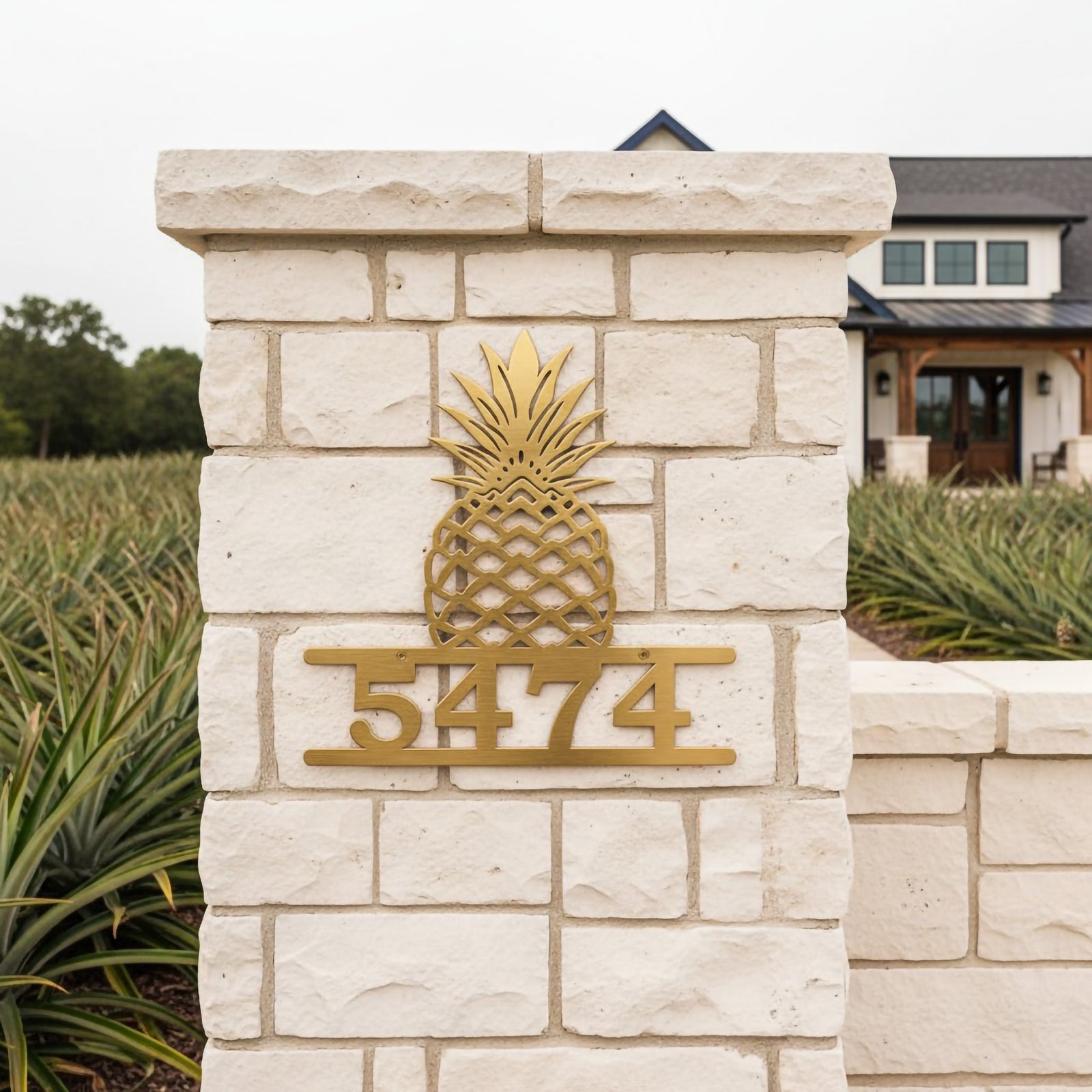 gold pineapple address sign with number 5474 mounted on a white stone pillar near a farmhouse entrance