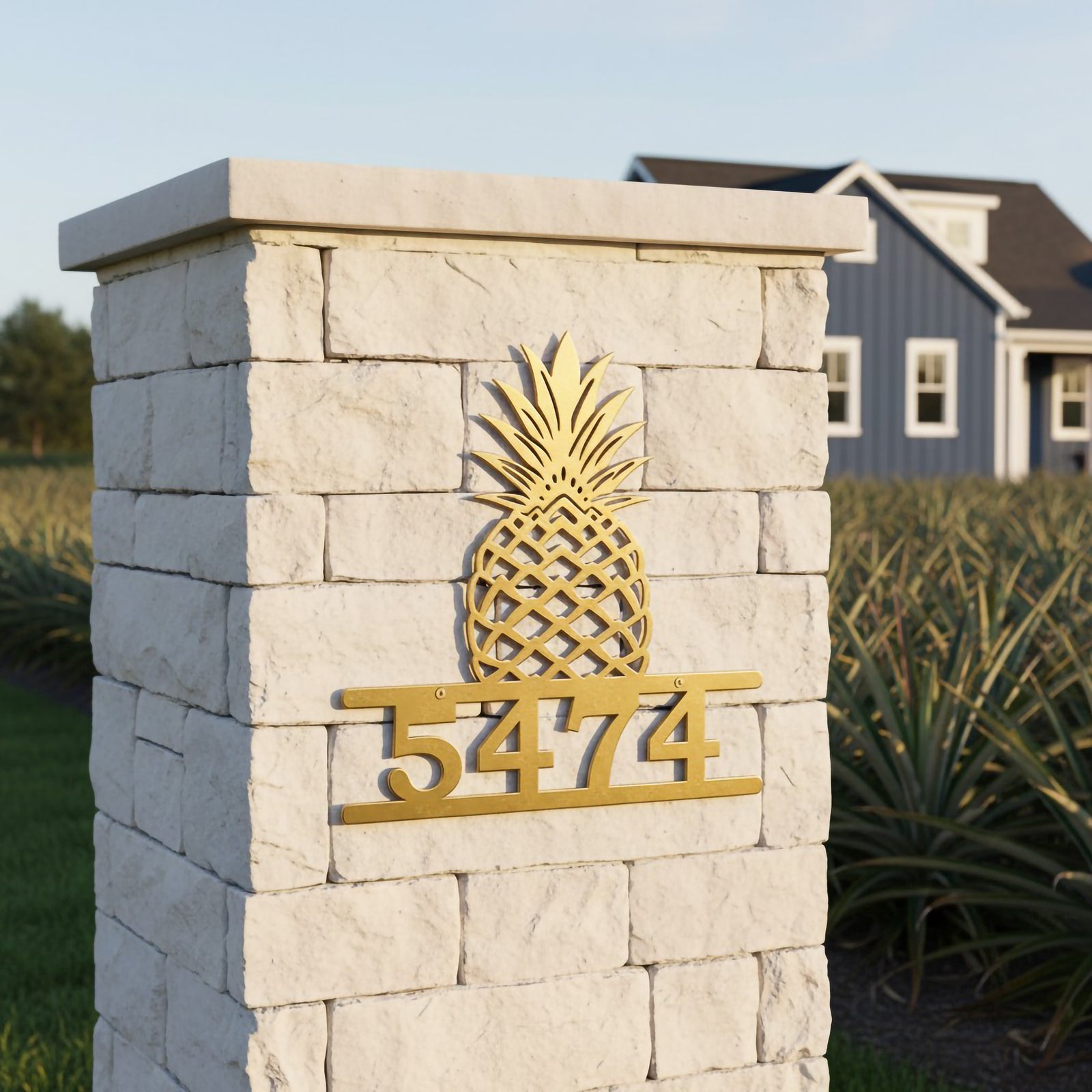 Gold pineapple metal house number sign with address 5474 displayed on a white stone gate pillar