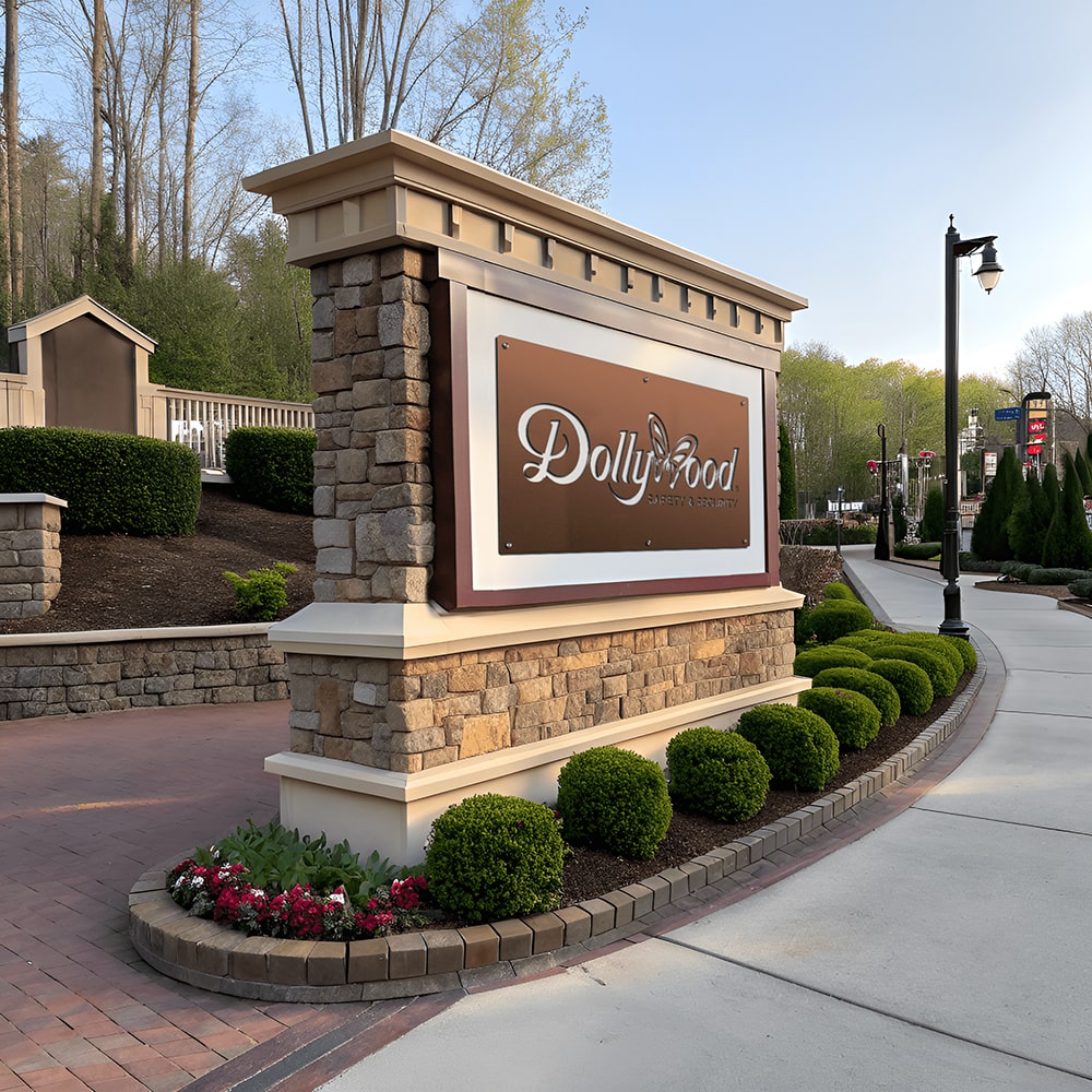 Large outdoor monument business sign with stone columns and landscaped base displayed along commercial property walkway and roadside entrance area