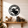 Black custom moose cabin metal wall sign displayed above wooden shelf with lantern books pinecones and lodge décor