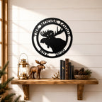 Black custom moose cabin metal wall sign displayed above wooden shelf with lantern books pinecones and lodge décor