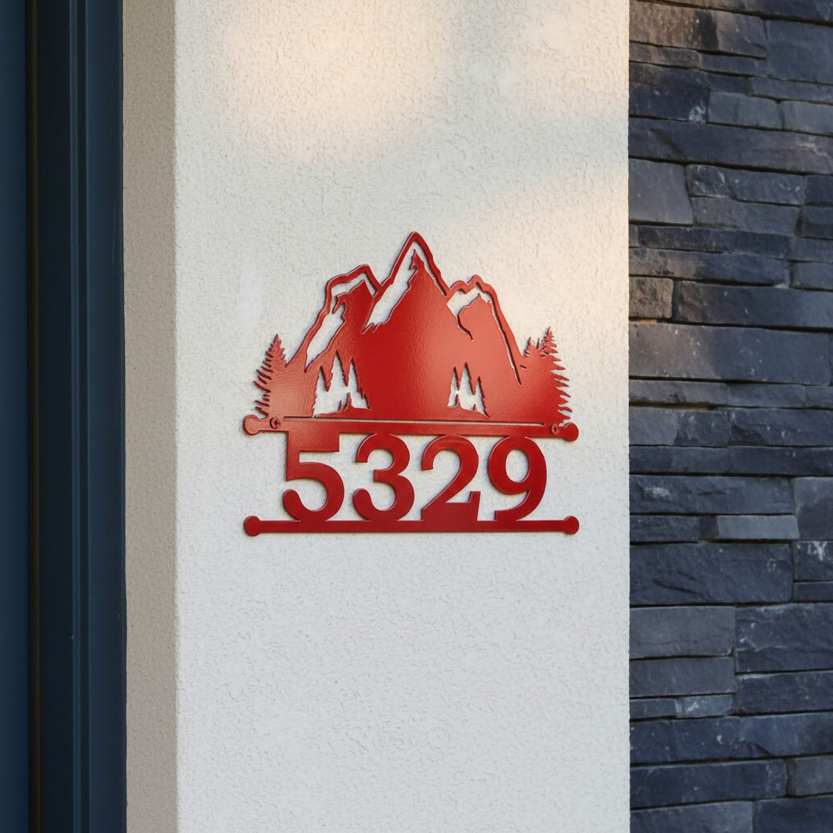 Red mountain metal address sign with 5329 displayed on a white stucco wall near dark stone siding