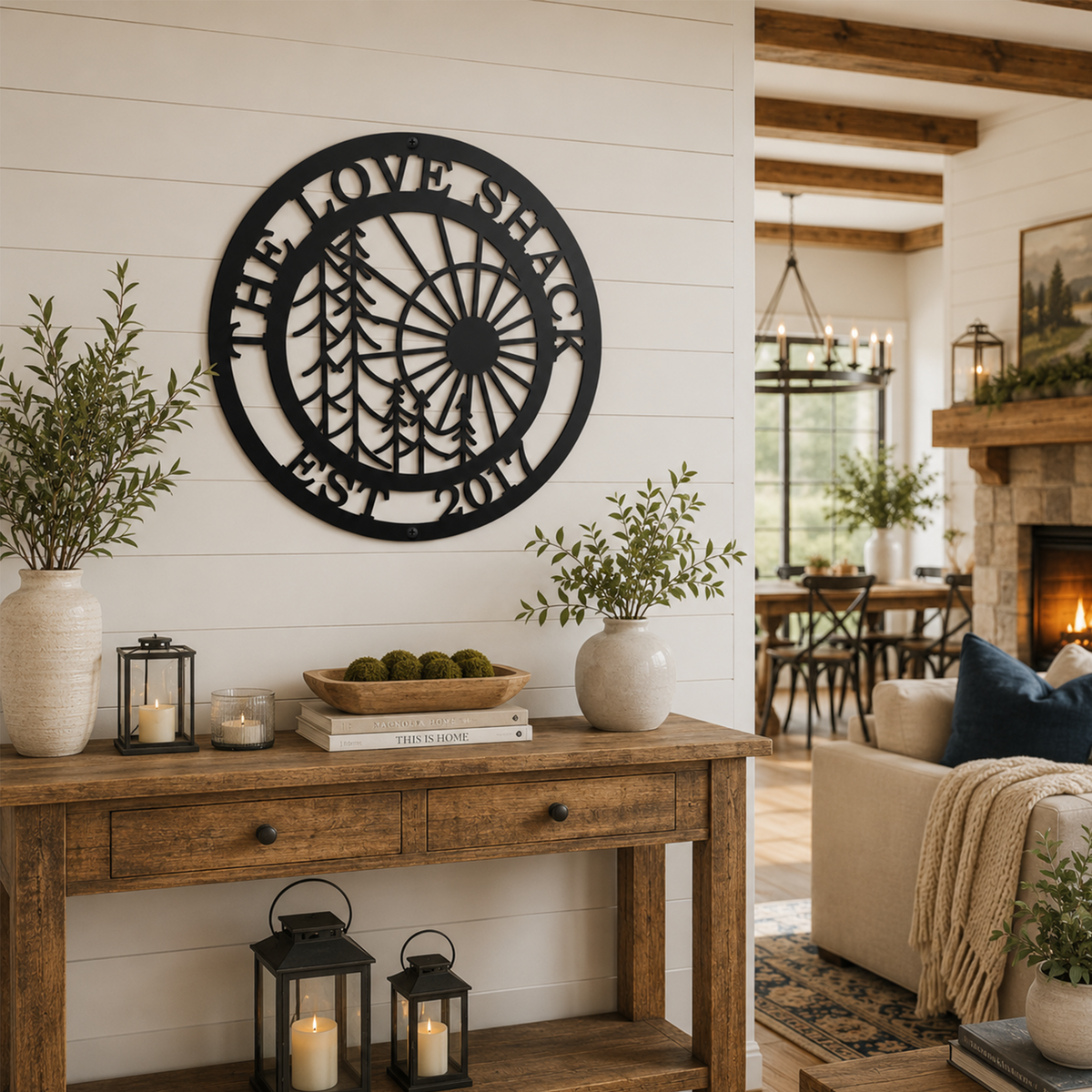 Black personalized family name metal wall sign with pine tree and sunrise design displayed above a rustic entryway console table in a modern farmhouse home