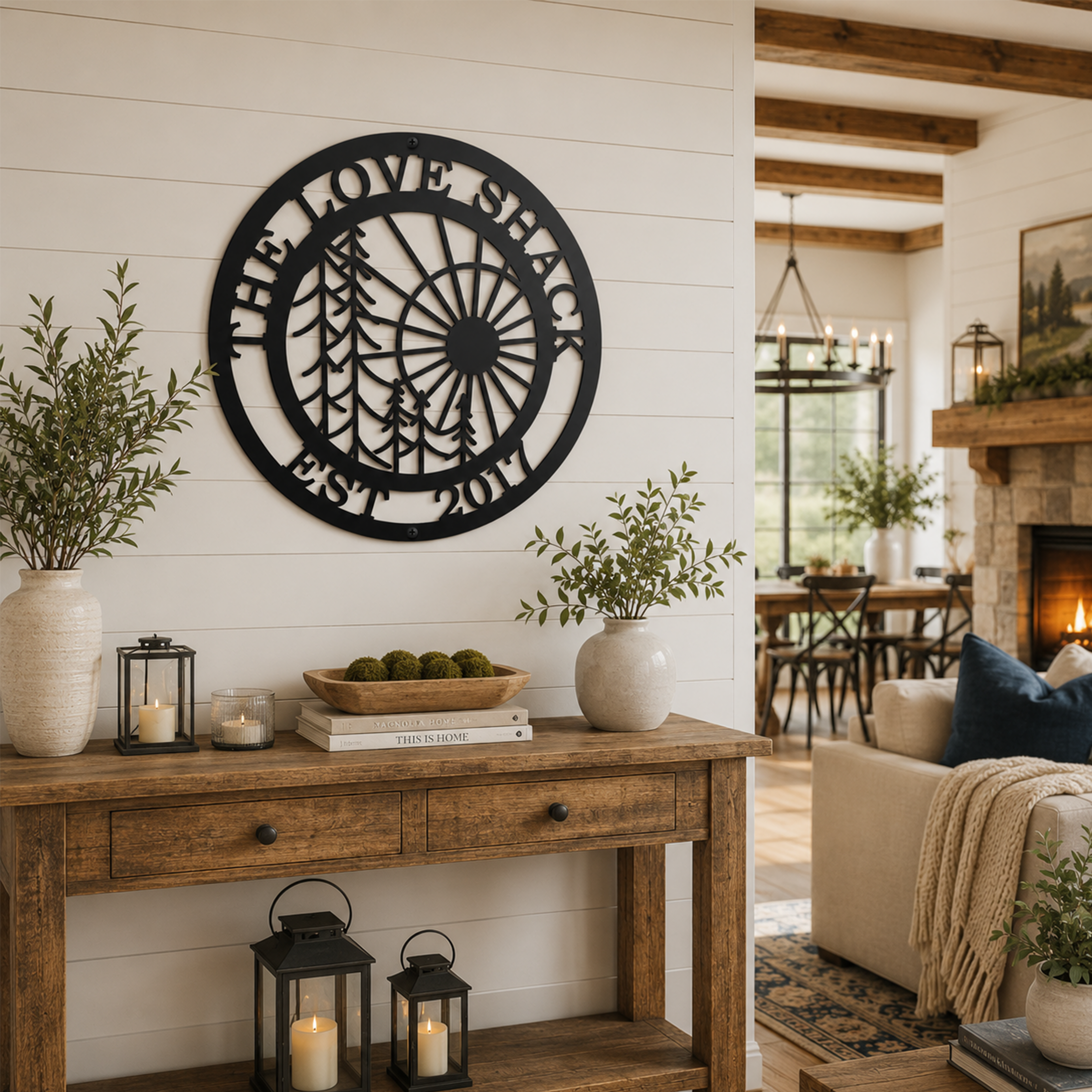 Black personalized family name metal wall sign with pine tree and sunrise design displayed above a rustic entryway console table in a modern farmhouse home