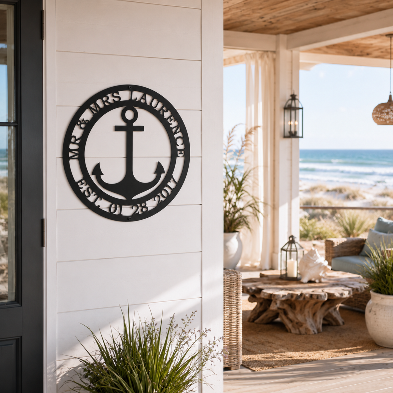 Black personalized wedding date anchor metal sign mounted on a white siding porch wall looking out to an outdoor deck with a driftwood table and beach scenery.