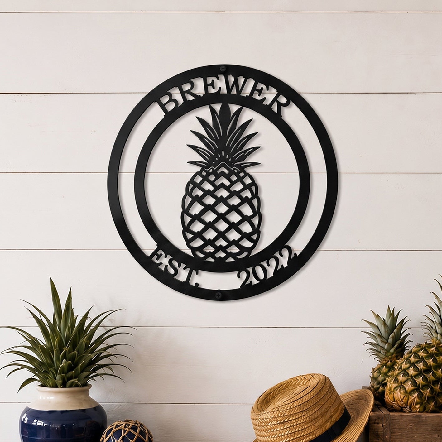 Black pineapple established family metal sign displayed above rustic wood table with pineapples and farmhouse decorations