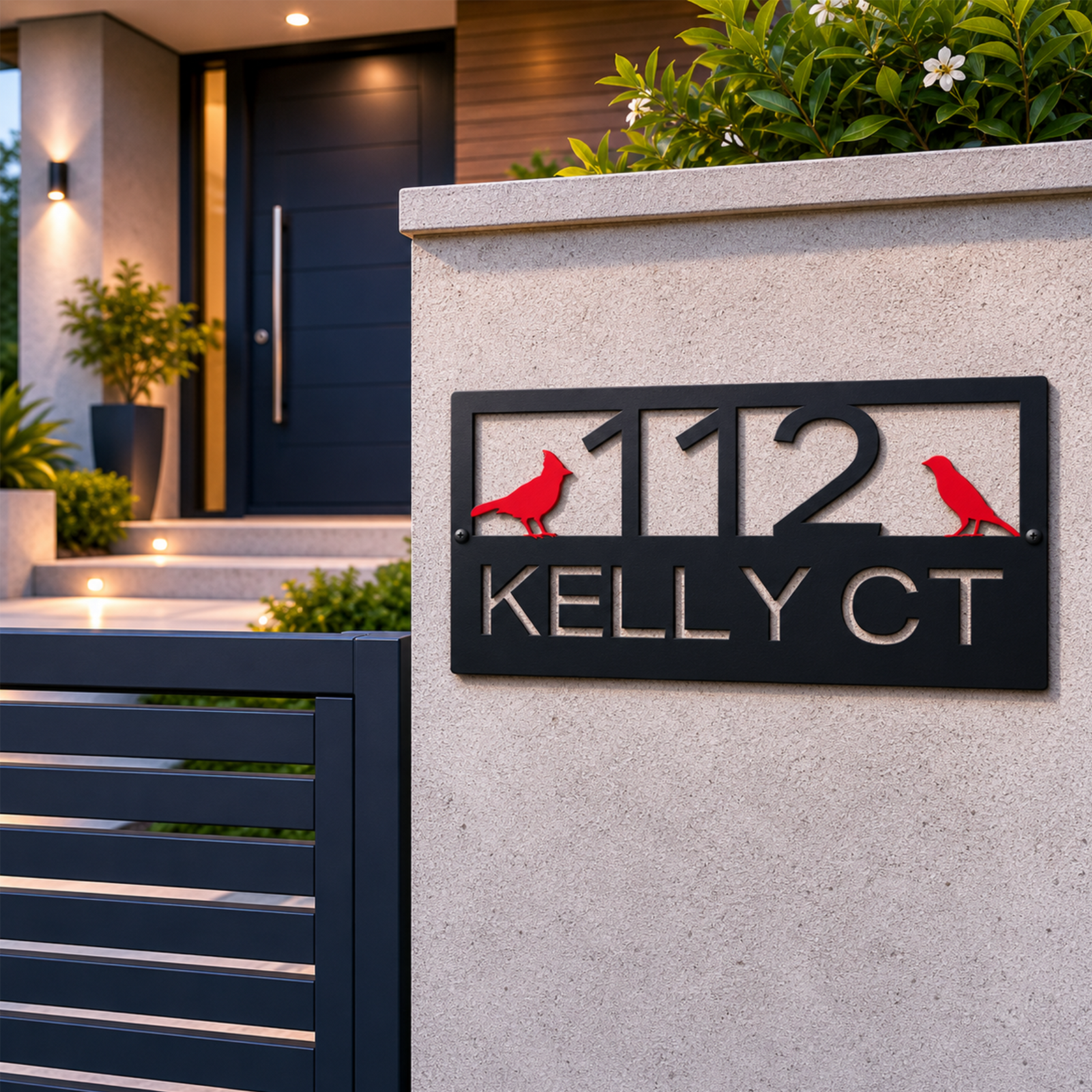 A high-contrast midnight black address sign featuring red cardinals and the text "112 KELLY CT" is installed on a modern concrete pillar. A sleek black gate runs along the bottom left corner, while soft exterior step lighting leads up to a contemporary dark wood accented front door.