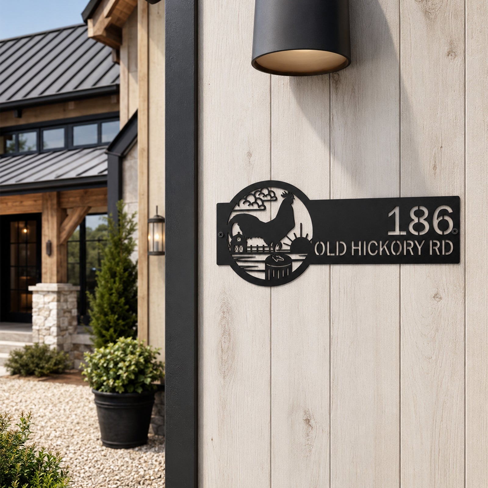 Black rooster ranch address metal sign mounted on light wood exterior wall featuring custom house number and farmhouse sunset landscape design
