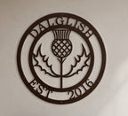 Close-up product shot of a dark espresso brown circular metal wall sign featuring a Scottish thistle flower design with custom name Dalglish and Est 2016.