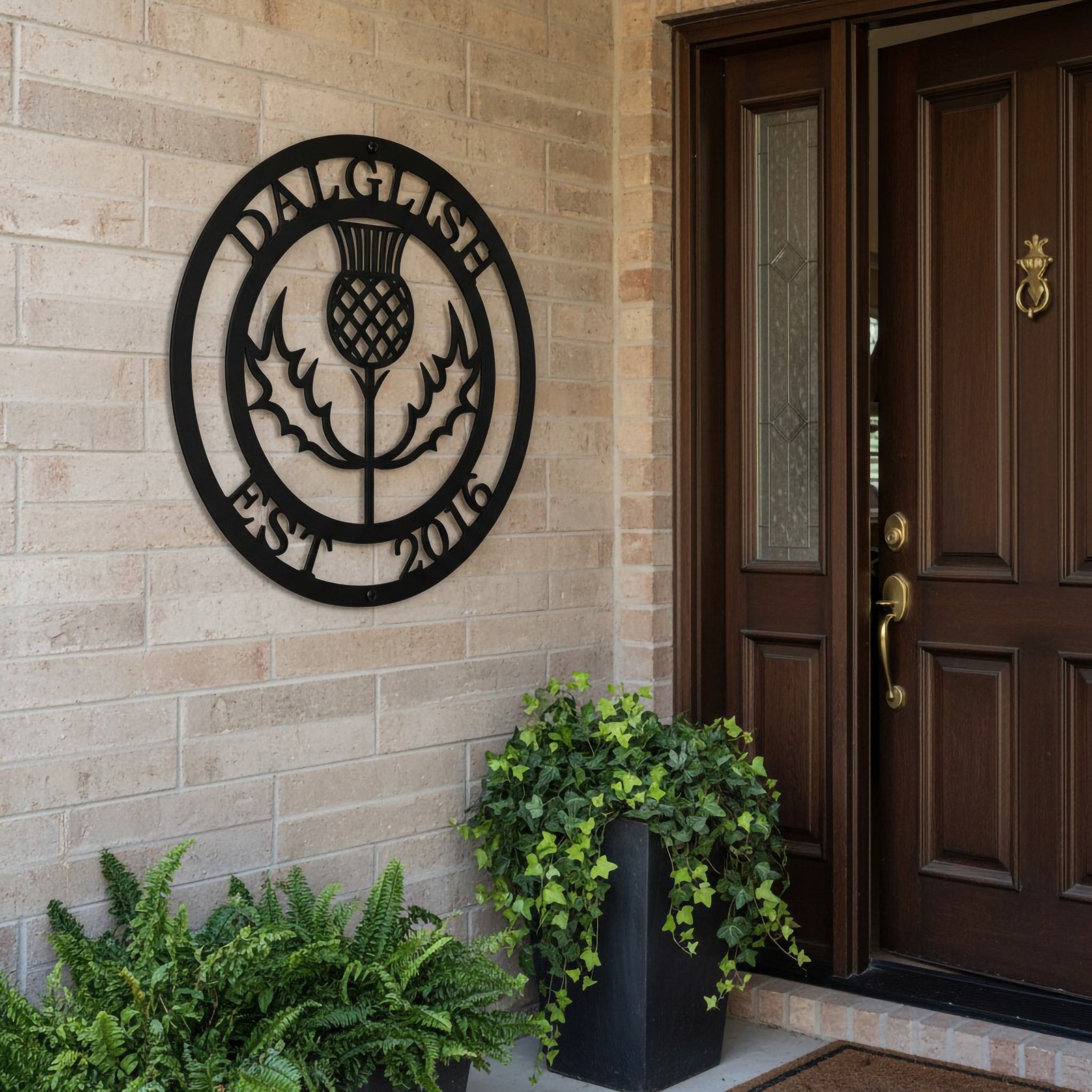 Satin black personalized Scottish thistle metal wall sign with family name Dalglish and Est 2016 mounted on a brick wall by a traditional wooden front door.