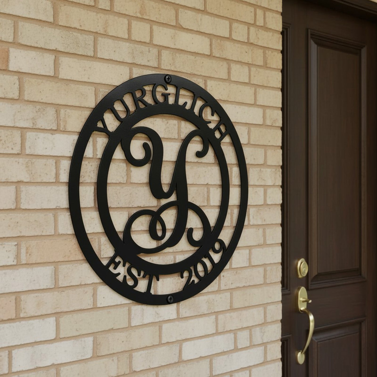 Satin black personalized metal monogram sign featuring a script letter Y with family name Yurglich and Est 2019 mounted on a light brick wall by a front door.