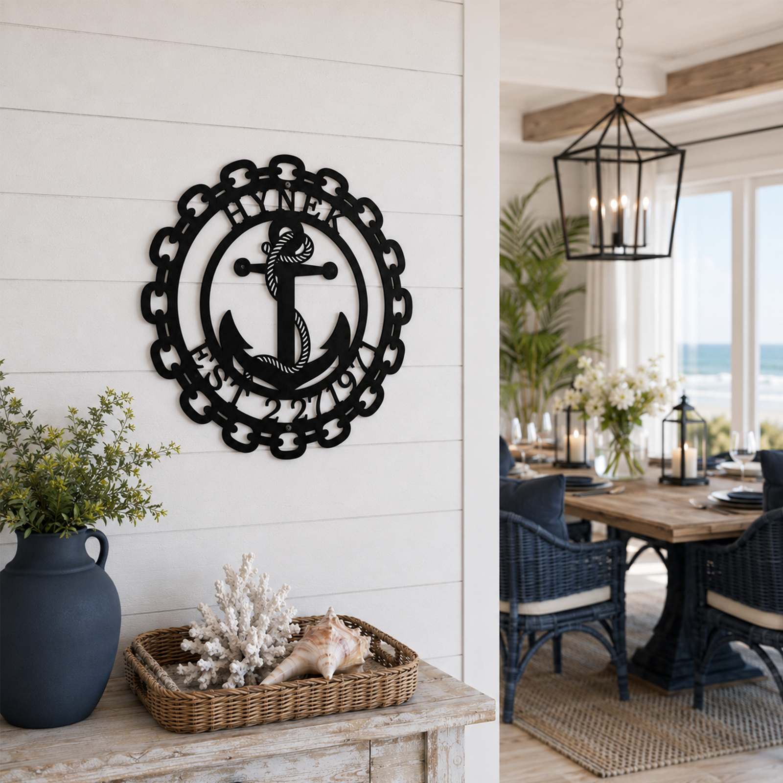 Custom black metal anchor wall decor featuring an outer chain border and personalized text, mounted on an entry wall next to a coastal dining room setting.