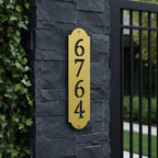 Spring yellow vertical address plaque with black cutout numbers mounted on a dark stone entrance pillar