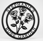 Flat view of a black circular personalized metal sign featuring a stylized three-rose bouquet cutout with the name layout over a pure white background.