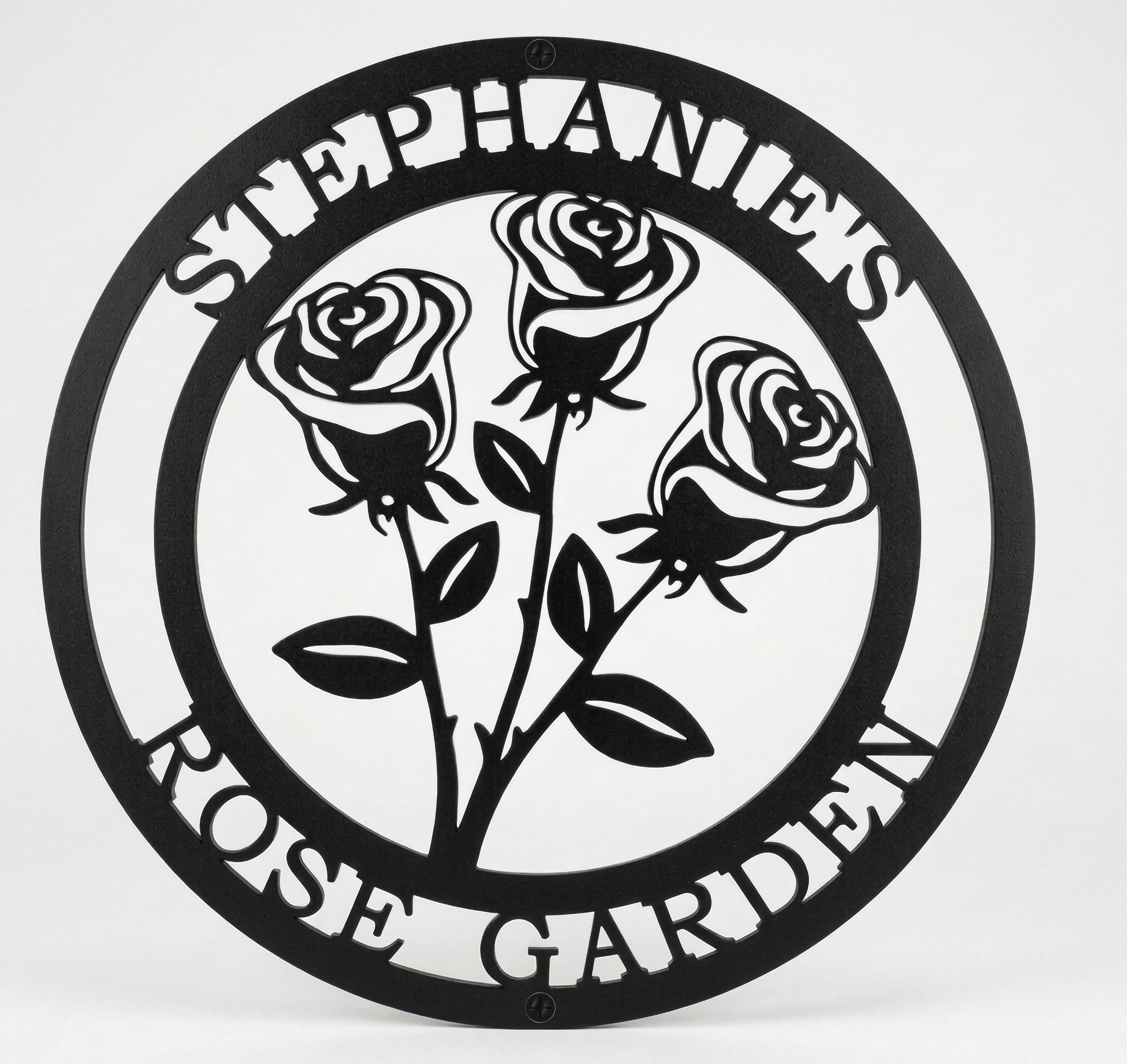 Flat view of a black circular personalized metal sign featuring a stylized three-rose bouquet cutout with the name layout over a pure white background.