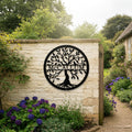 Large black round metal tree of life monogram sign featuring the name McCallum hung on a rustic cream stone wall next to an open wooden gate and a gravel garden pathway.