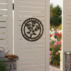 Satin black personalized botanical rose bouquet metal sign with custom text Stephanie's Rose Garden mounted centrally on a white slatted privacy gate overlooking a flower bed.