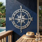 White compass rose metal sign with custom coordinates and beach name displayed on a blue outdoor patio wall
