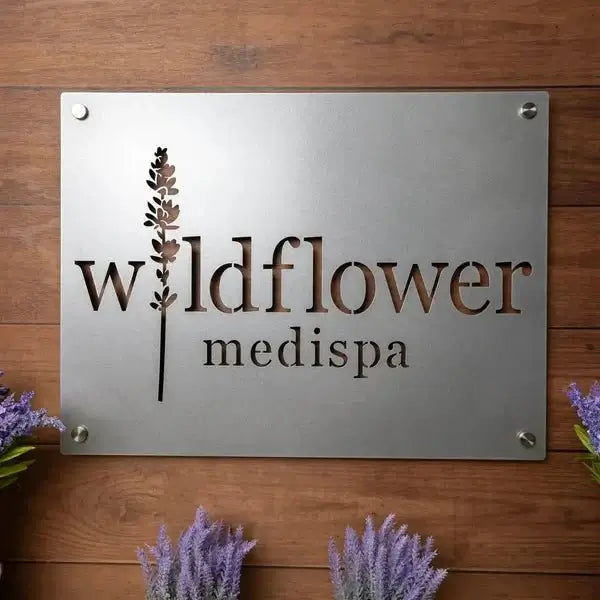 Brushed silver custom wildflower medispa metal business sign with floral logo mounted on wooden wall with decorative lavender flowers for spa office or salon decor
