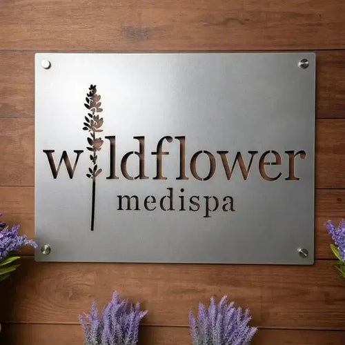 Brushed silver custom wildflower medispa metal business sign with floral logo mounted on wooden wall with decorative lavender flowers for spa office or salon decor