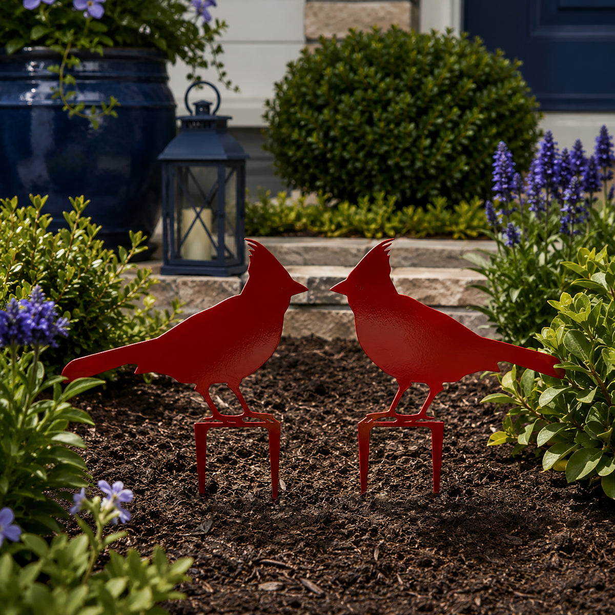 Deep red cardinal metal yard stakes placed in garden mulch near front porch flowers and greenery