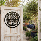  black circular metal tree sign stating "The Burkes Welcome Est. 2011," mounted on a rustic, weathered white wooden door that opens into a bright glass greenhouse filled with plants.