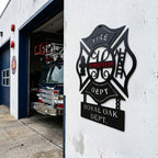 Custom firefighter maltese cross metal wall sign mounted outside fire station with fire truck in garage background