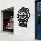 Black firefighter maltese cross metal sign displayed outside fire station beside fire engine bay and blue door