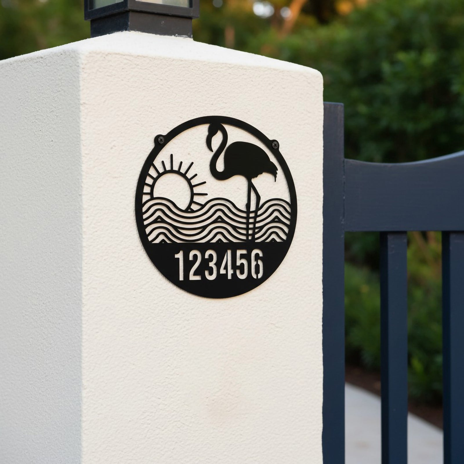 Gloss black round flamingo address plaque with number 123456 mounted on stucco gate post