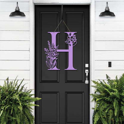 Metal Floral Monogram Door Wreath displayed on a black door, showcasing a personalized letter surrounded by intricate floral designs, ideal for front doors or gardens. Perfect for weddings and housewarmings.