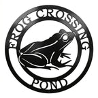 Black frog crossing pond metal wall art sign with circular nature design on white background