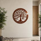 A circular metal sign with a shiny metallic Tuscan copper finish depicting a detailed Tree of Life cutout. The outer ring is engraved with an inspirational circle of life quote. It is mounted on a large off-white wall in a modern room with a light wood door, an indoor plant, and a river stone floor border.