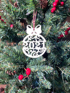 Red gift box metal Christmas ornament displayed on decorated Christmas tree with pine branches